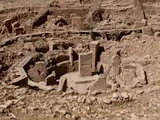Site archéologique avec des structures en pierre et des colonnes, entouré de terre et de rochers.