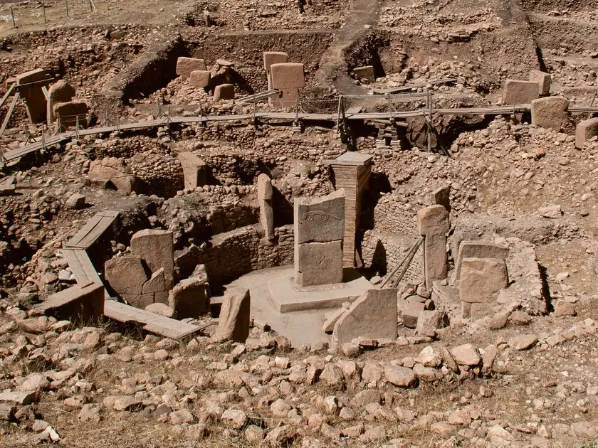 Site archéologique avec des structures en pierre et des colonnes, entouré de terre et de rochers.