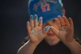 Un enfant avec un chapeau bleu montre ses mains couvertes de peinture.